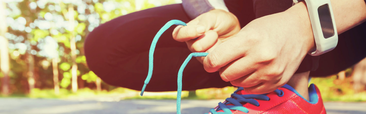 Female joffer tying her running shoes for a jog with a smartwatch on her wrist