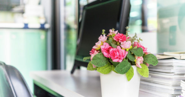 A desk with a thick stack of papers and a fake potted plant near the edge of the desk