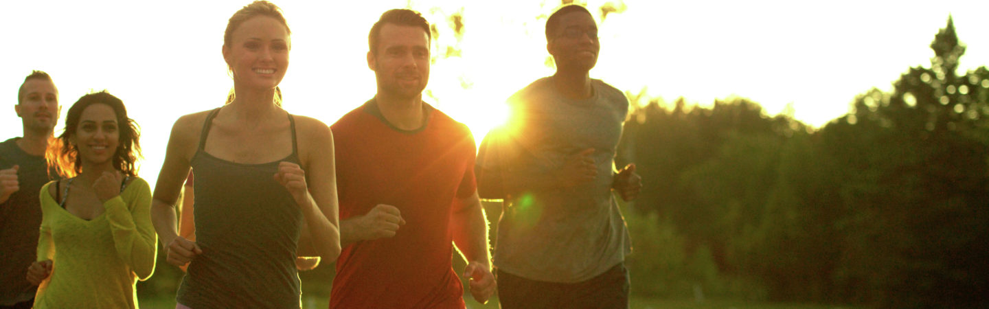 A group of men and women jogging outdoors on a path while backlit by the sun