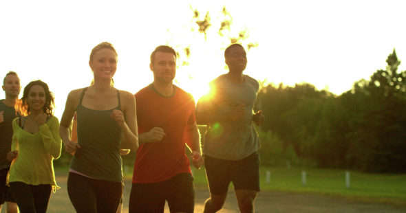 A group of men and women jogging outdoors on a path while backlit by the sun