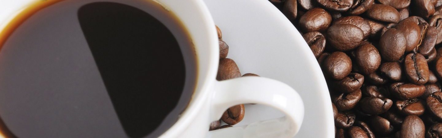 A cup of coffee on a small plate surrounded by whole coffee beans