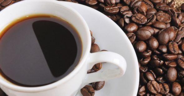 A cup of coffee on a small plate surrounded by whole coffee beans