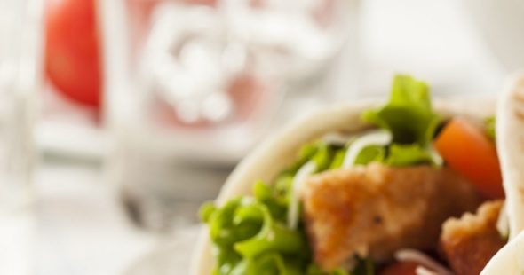 A healthy chicken wrap sandwich wuith tomatos, lettuce and shredded cheese