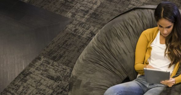 A young woman in a yellow cardigan sitting in a bean bag and using a tablet
