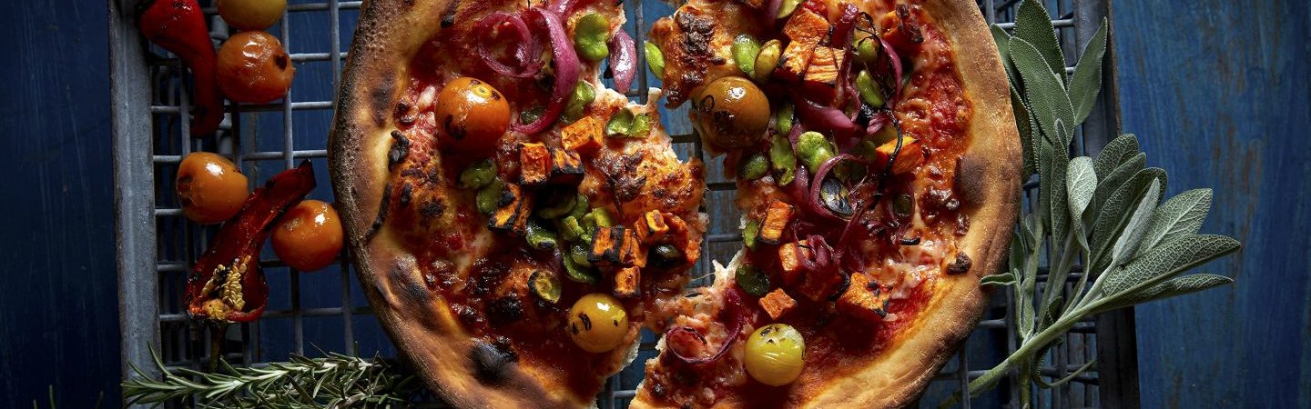 Photography of a thin crust pizza topped with heirloom tomatoes and accented with fresh herbs and peppers