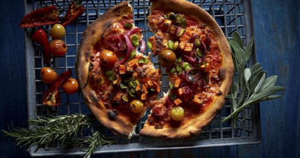Photography of a thin crust pizza topped with heirloom tomatoes and accented with fresh herbs and peppers