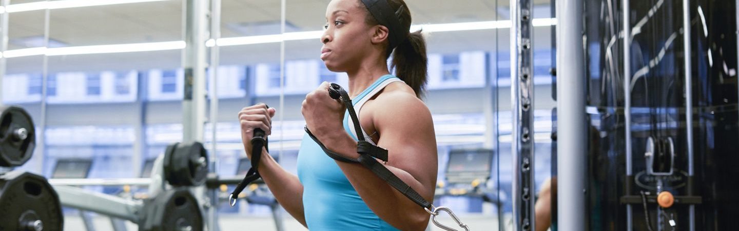 A fit woman listing weights at a KINETIC fitness center