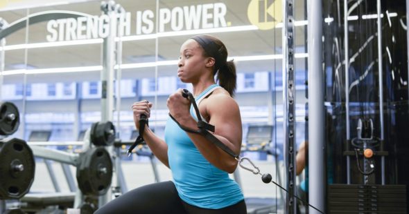 A fit woman listing weights at a KINETIC fitness center