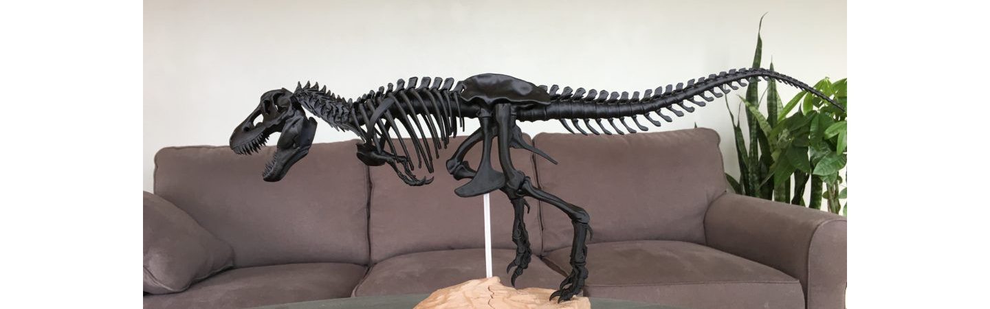 3D printed tyrannosaurus rex model on a wooden table with a suede couch in the background