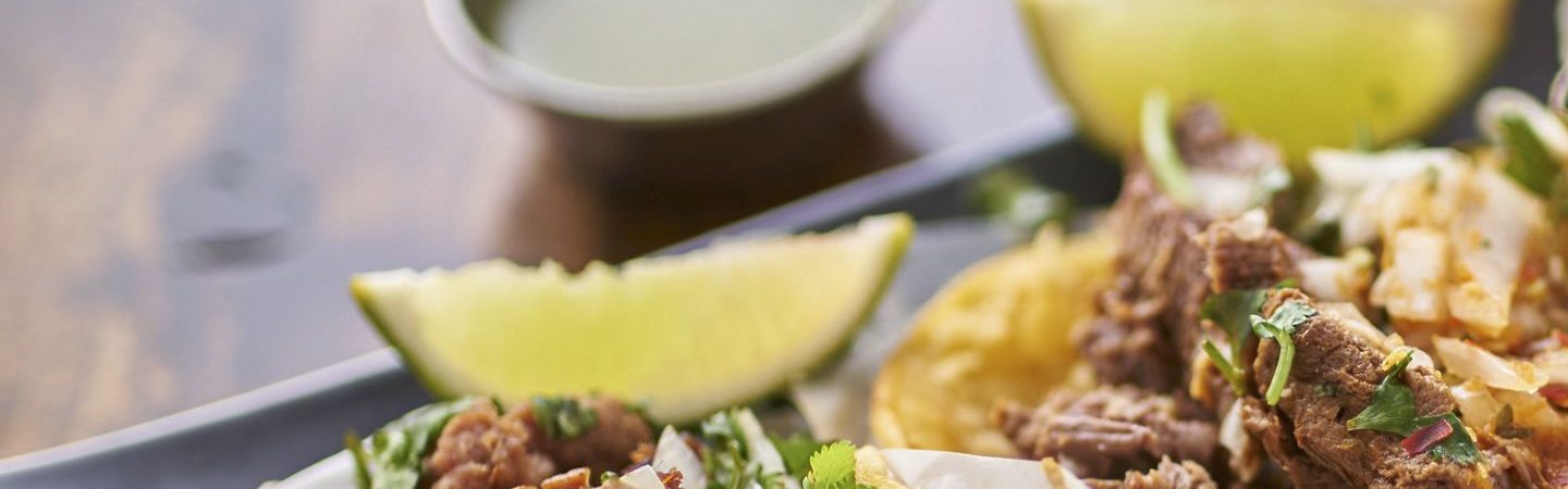 Corn tortilla tacos topped with shredded meat, onions, and cilantro