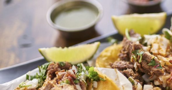 Corn tortilla tacos topped with shredded meat, onions, and cilantro