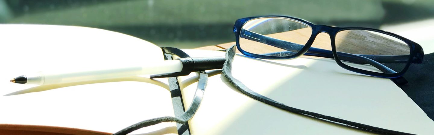 Photography of a pair of glasses, a ballpoint pen and open journal