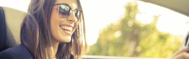 Woman wearing sunglasses and smiling while driving a convertible