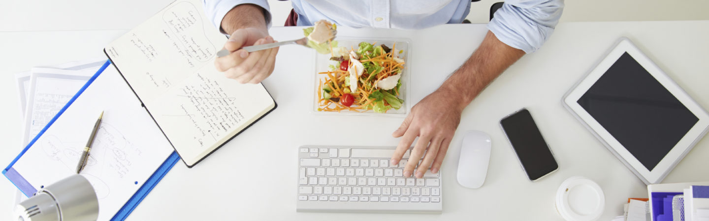 Woman eating lunch and working at her desk at the same time