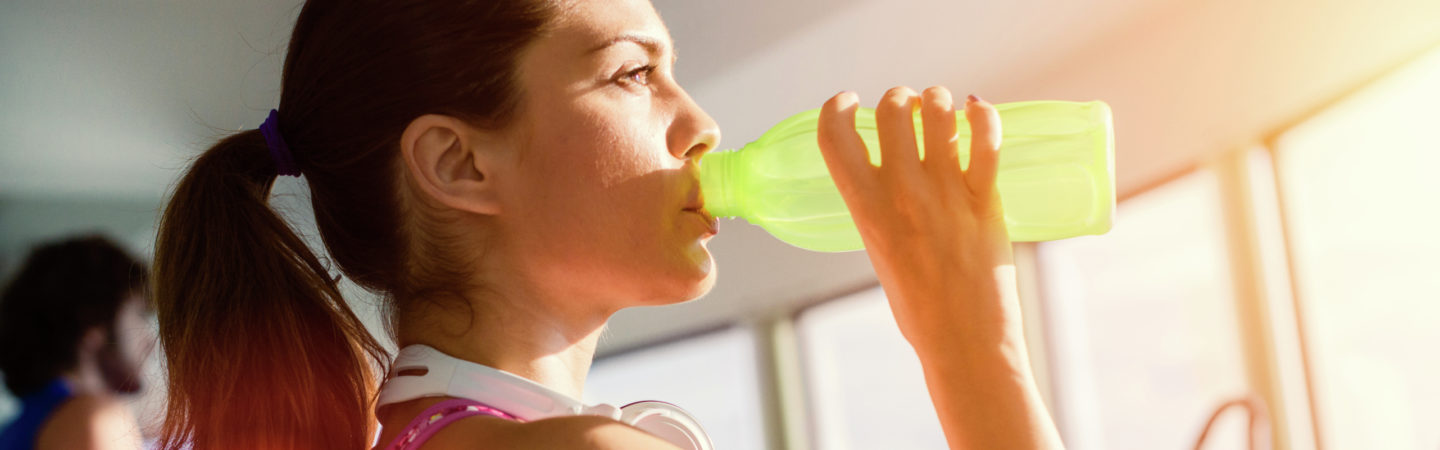 Young woman drinking water from a green bottle while working out