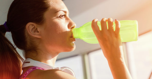 Young woman drinking water from a green bottle while working out