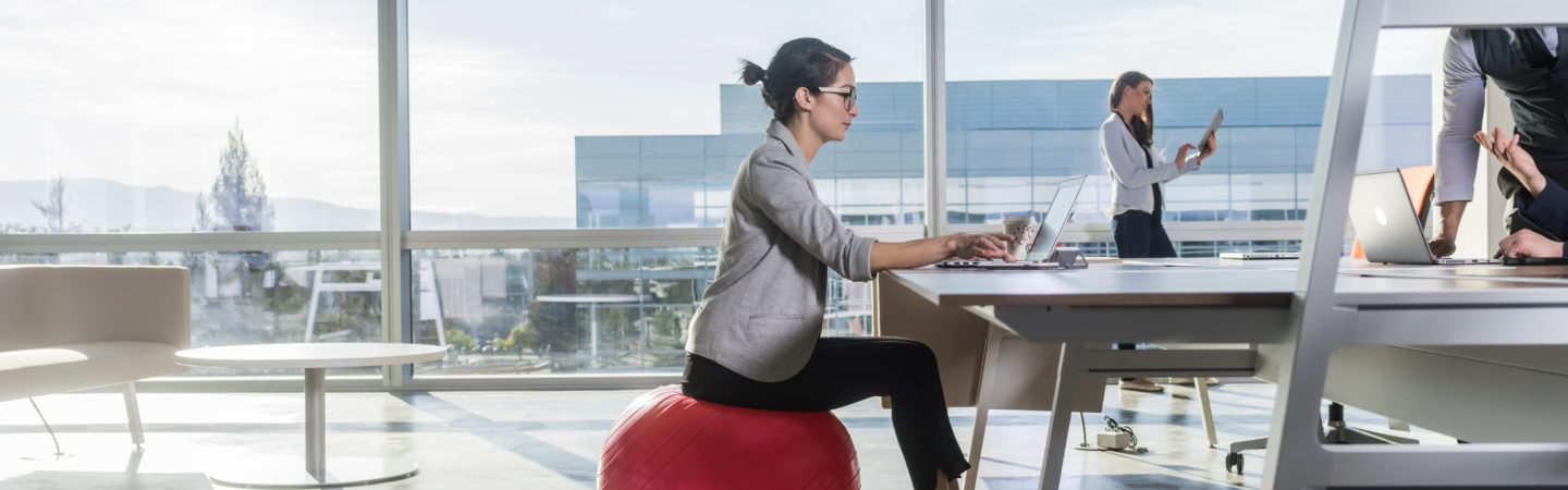 Woman sitting on a yoga ball at her desk with KINETIC®branded weights nearby