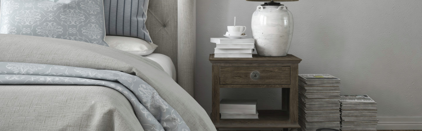 Photography of a bedroom and nightstand with a lamp, a stack of books, and a cup of coffee