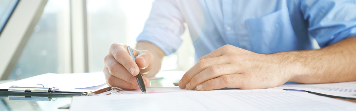 Man in a blue shirt holding a pen doing paperwork over a reflective table